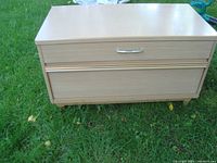 Front view of blonde wood dresser showing two drawers and bamboo-style metal handle on top drawer.
