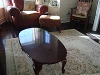 Oval wooden coffee table with shiny polished surface in a living room setting near a red armchair and ottoman.