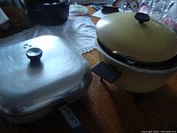 Photo showing vintage round beige deep fryer with lid and black knob handle, sitting on table.