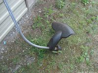 Close-up of the cutting head and protective guard on the curved shaft of the weed wacker, showing wear and dirt from use.