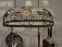 Front view of the hanging pots and pan holder rack showing the ornamental metal scrollwork and floral centerpiece with pots hanging from the hooks