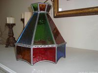 Tapered hexagonal pendant light made with colorful stained glass panels framed in lead came, showing the red, green, blue, and amber panes and scalloped bottom edge.