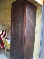 Full view of the tall wooden cupboard showing the side and front door, highlighting the wood grain and condition.