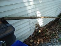 Full length image of the large wooden board leaning against white siding showing dirt and natural weathering.