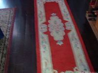 Full length view of the red wool runner rug displaying the floral center pattern and decorative borders on a dark wood floor.