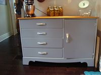 Front view of renovated sideboard painted light gray with four drawers to the left, each with white handles, and a natural wood top.