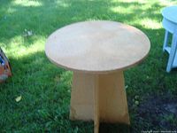 Photo of small round side table with solid pedestal base shown outdoors on grass.