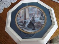 Framed round collectible plate with a winter Christmas scene in muted tones and blue frame mat with gold trim