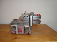 Side view of vintage metal wind-up dog toy showing riveted metal construction and mouth detail.