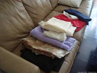 Stack of folded fabric pieces in multiple colors including black, floral pattern, lavender, cream, red, and navy blue, placed on a brown couch.