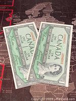 Two consecutive 1954 Canadian one dollar banknotes laid out flat showing front side with Queen Elizabeth II portrait and serial numbers.