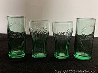 Photo showing set of 4 green Coca-Cola glasses including 2 taller with 'Property of Coca-Cola Atlanta GA' embossed text and 2 shorter Coca-Cola logo embossed glasses.