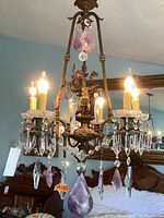 Full view of chandelier hung, showing brass frame, crystal prisms, candle lights and purple glass accents