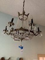 Full profile photo of the chandelier hanging from the ceiling showing brass arms, crystal beads, and 6 candle-style light sockets with no bulbs installed.