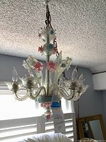 Full view of the pink, blue, and yellow floral glass chandelier hanging from ceiling chain with multiple arms and candle-like bulbs.