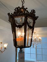 Front view of hanging ornate metal and glass light fixture with two lit bulbs inside.