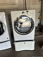White Whirlpool gas dryer with large front window door and partially open pedestal drawer beneath, showing its condition and setup.