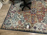 Full view of the rug showing the complex colorful pattern and part of office chair base on rug.