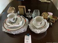 Photo showing assorted Christmas-themed dishes including stacked plates and cups along with additional kitchen and decorative containers arranged on a dark table.