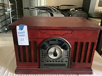 Front view showing the wooden cabinet with retro speaker grille and central analogue radio dial with digital display and buttons.
