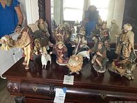 Full set of twelve porcelain nativity figure pieces arranged on wooden table including baby Jesus, Mary, Joseph, wise men, shepherd, camel, and sheep