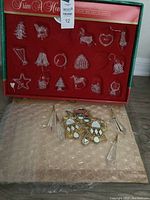 Box of handmade spun glass Christmas tree ornaments with some slots empty for missing pieces. Set is in original display box with red interior and green outer box labeled Trim A Home.