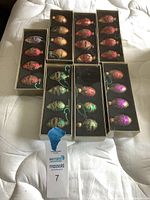 Seven unopened boxes of Christmas tree ornaments with six teardrop-shaped decorations each, featuring various colors and decorative swirl patterns.