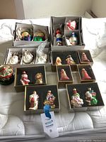 Photo shows a collection of boxed Christmas ornaments including Santa Claus figures, bell ornaments, lighthouse, fish, and carousel style pieces.