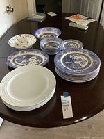 Photo showing grouped blue and white patterned plates and bowls alongside plain white plates on a dark wooden table.