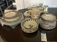 Overall view of assorted dishware including plates, bowls, cups, and pitchers with decorative fruit and bird motifs.