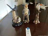 Three decorative figurines, shown on table: two birds and one human figure.