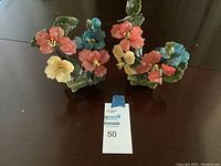 Two glass flower decorative pieces with colorful flowers and green leaves on a dark surface.