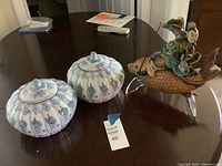 Two white porcelain jars with blue and green floral designs and an Asian figurine on a fish next to them on a table.