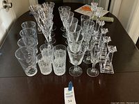 Wide angle view of the assorted clear glassware collection showing rows of various glasses and candlesticks on a dark table.
