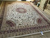 Full view of large rectangular patterned area rug with central floral medallion on light background placed on wooden floor.