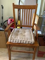 Front view of wooden arm chair with beige tufted cushion placed on seat, showing design and condition with visible scratches and marks.