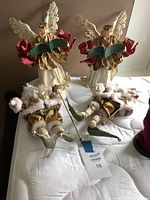 Photo of two standing paper mache angels and two seated Santa figurines on a white surface.