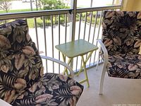 Two patio chairs with floral cushions and a small green folding table on a balcony