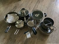 Full set of assorted pots and pans laid out on floor showing all items and lids.