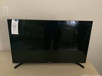 Front view of Samsung flat screen TV showing black bezel, two V-shaped stands, and screen in off state.