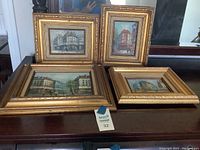 Four vintage framed paintings showing different urban scenes on canvas, artist signature visible.