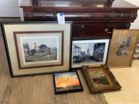 Set of five artworks arranged on the floor including horse riding scene, street scene, Asian-style woman painting, sunset birds, and ornate framed oil painting.