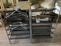 Two black metal shoe racks side by side with mesh shelving. Several plastic and wooden hangers are resting on the racks.