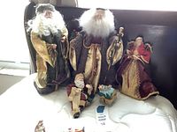 Five traditional Santa Claus figurines and small house figurine arranged on mattress, showing fabric costumes and details