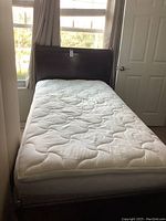 Full view of twin bed complete with mattress set against window and door.