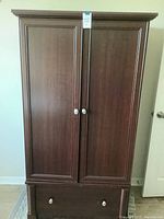 Closed view of wooden wardrobe showing two paneled doors with round knobs and a bottom drawer with similar knobs.