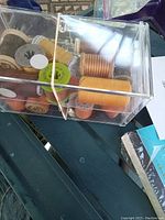 Top view of transparent plastic box containing multiple vintage sewing threads mostly in orange and brown colors on various wooden and plastic spools.
