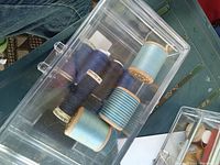 Clear plastic case with assorted blue thread spools on wooden cores, showing various thread shades
