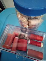 Plastic jar filled with wooden and plastic thread spools in beige and light shades resting on a blue surface.