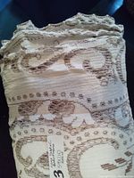 White folded lace fabric with floral and swirl lace embroidery and a handwritten tag showing measurements 59x110 inches